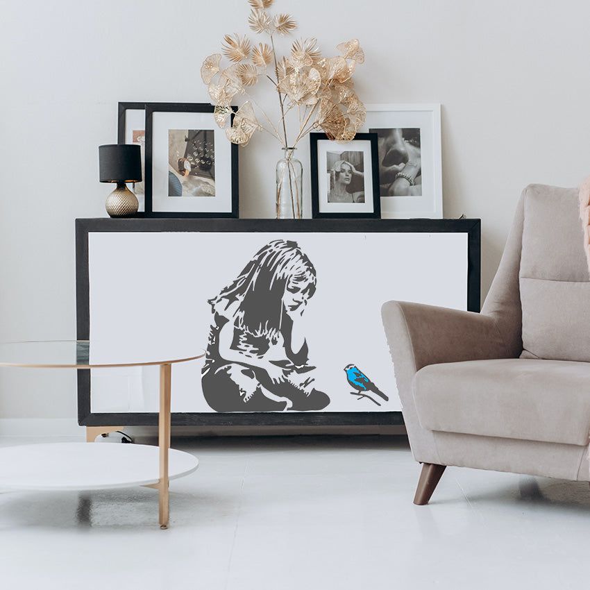 A living room with a Banksy Blue Bird Little Girl sitting on a chair.